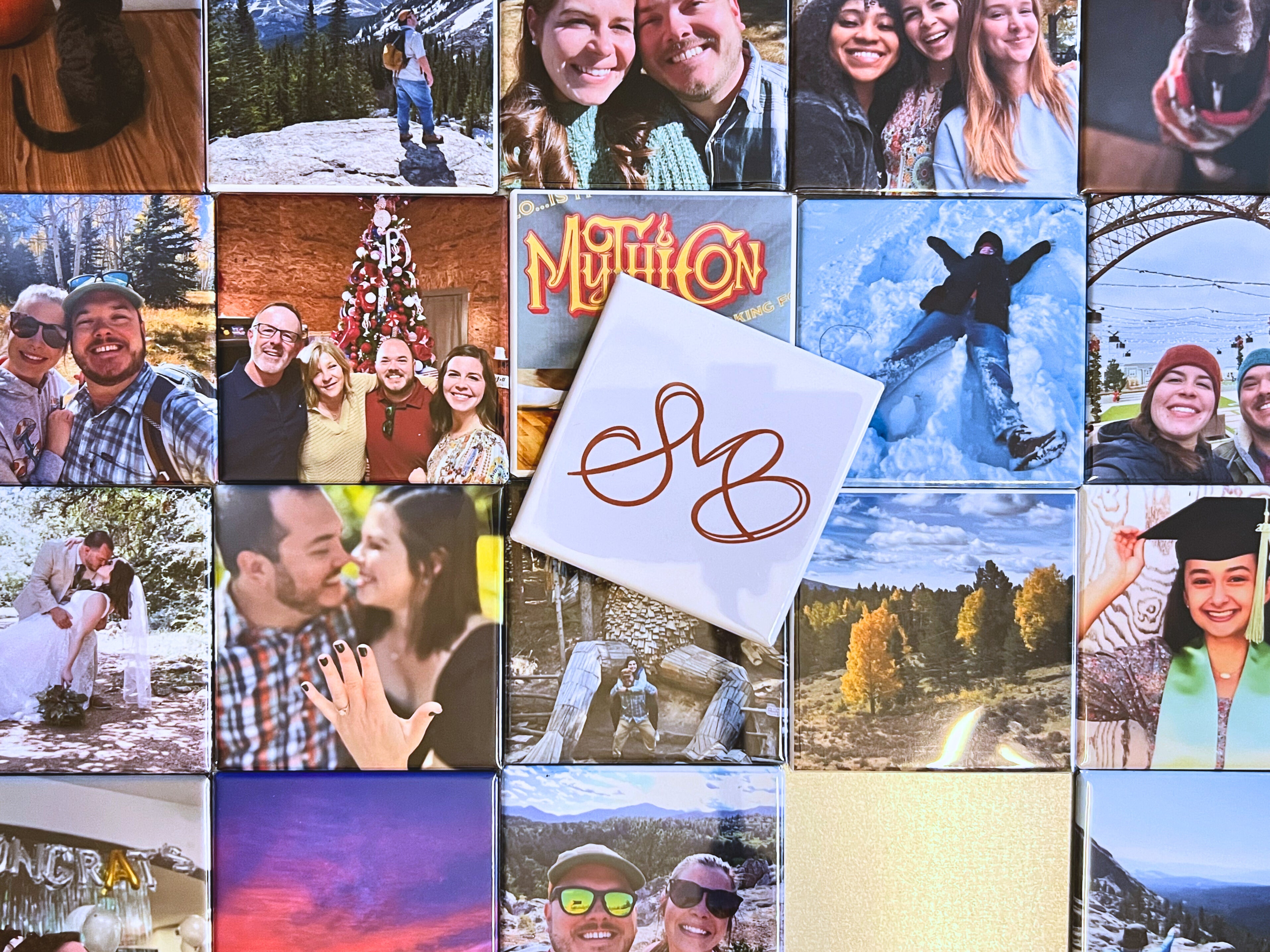A grid of 2.5-inch square custom photo magnets displaying personal memories — hiking trips, family holidays, weddings, engagements, and graduations — arranged in a mosaic on a flat surface, with a white Spellbound Magnet Co. logo magnet displayed in the center.